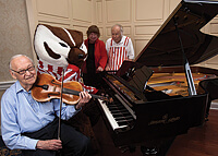 Cultural events are key at the Capitol Lakes retirement center. From left, resident Jim Crow, a UW-Madison emeritus professor of genetics, plays his viola, while Bucky Badger demonstrates his piano skills for residents Janice and Jean-Pierre Golay. Photo: Andy Manis