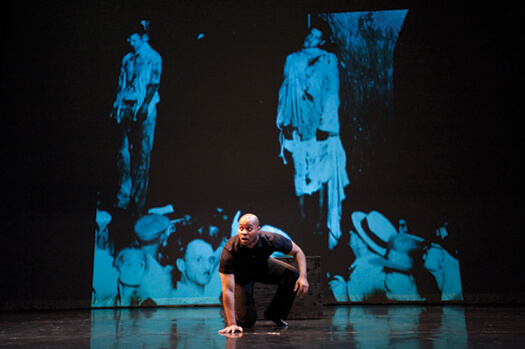 <p>Fear takes center stage: In his one-man play Ten Perfect, Patrick Sims portrays a fictionalized version of James Cameron, who was nearly lynched in Marion, Indiana, in 1930. Two other men were murdered that night, and the act was captured in an iconic photo (shown in the background) that inspired the lyrics to “Strange Fruit.” Photo: Jeff Miller</p>