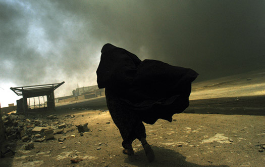 An Iraqi woman walks through a plume of smoke