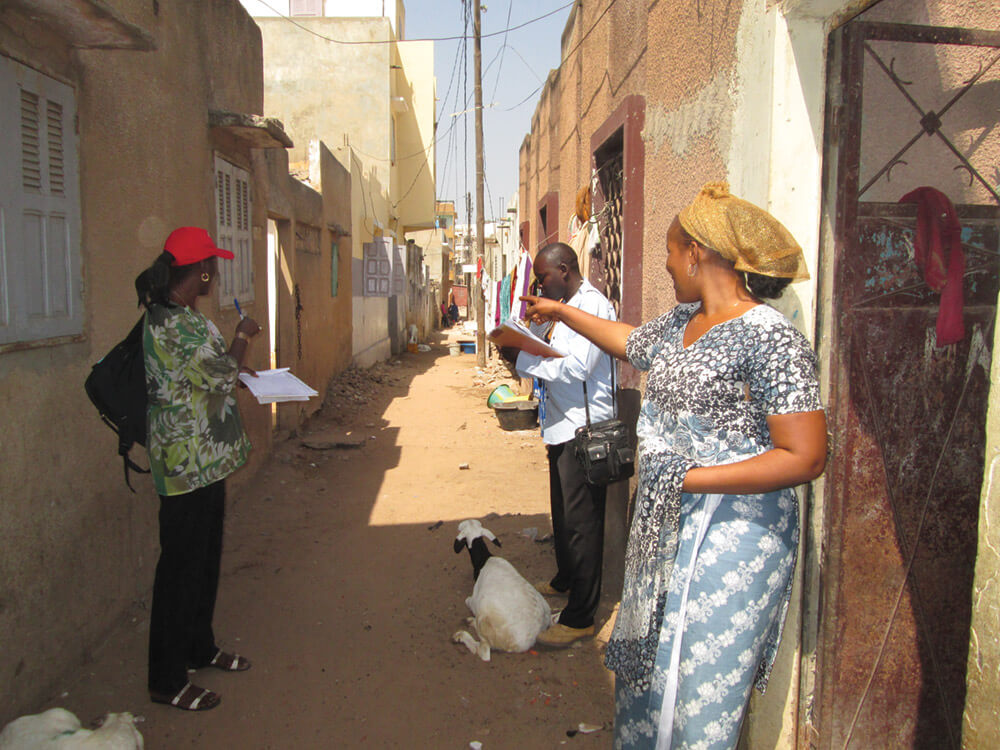 During a sanitation baseline survey to determine what desludging systems residents are currently using, survey-team members  get directions to the next respondent’s house from a woman (right) whom they  just finished interviewing. Photo: Ahmadou Kandji.