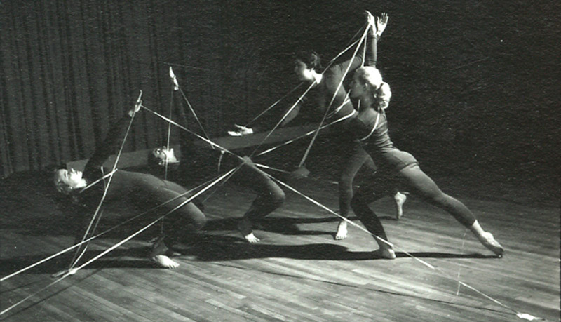 Black and white photo of four women wearing black unitards doing a modern dance routine.