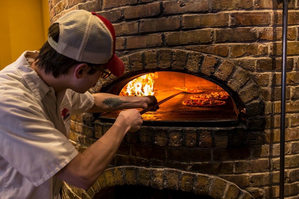 Employee places pizza inside the wood-fired oven at Pizza Brutta