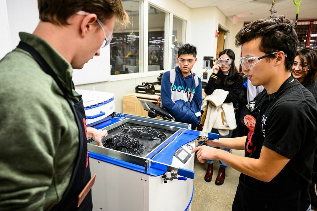 Students wearing safety goggles work on a machine