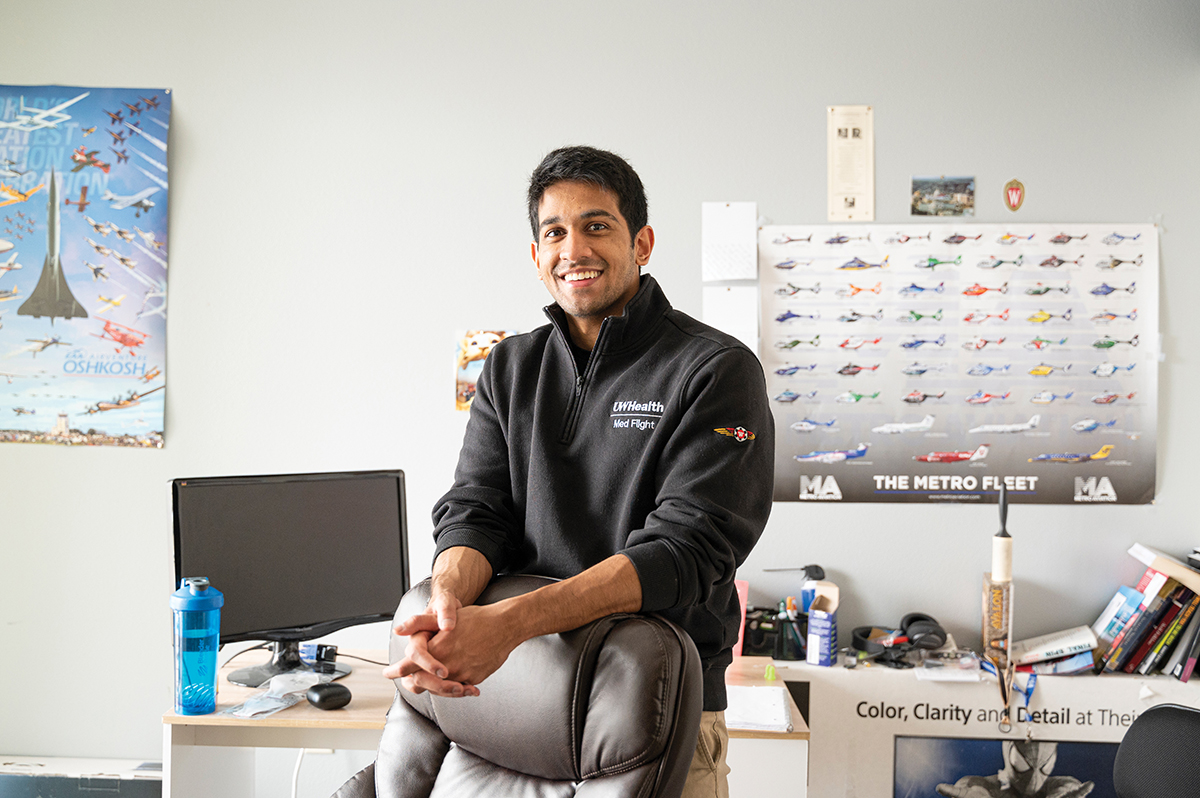 Tikiri Bandara sits in front of his desk over which is a poster featuring different helicopter types