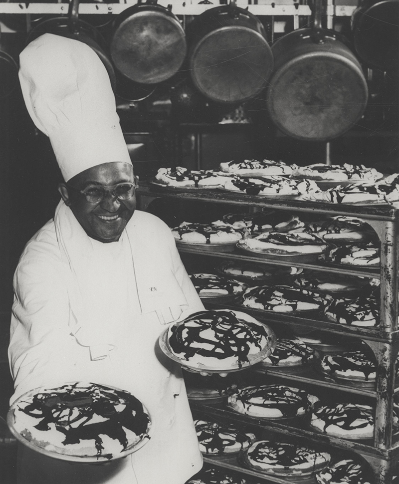 Black and white photo of Carson Gulley in a tall chef's hat holding two fudge-bottom pies