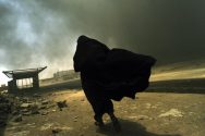 An Iraqi woman walks through a plume of smoke