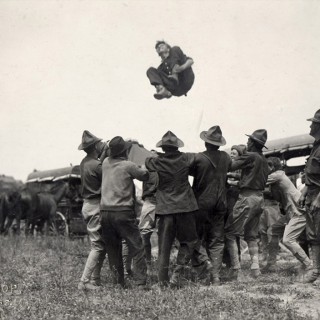 A group of World War I-era student cadets bounces a new recruit in the air during an initiation ritual. “The University is reorganized on a war basis and is now in full operation as a military institution so far as the S.A.T.C. students are concerned,” acting UW President E.A. Birge said of the Student Army Training Corps in a talk to alumni in Chicago in 1918. <span class=