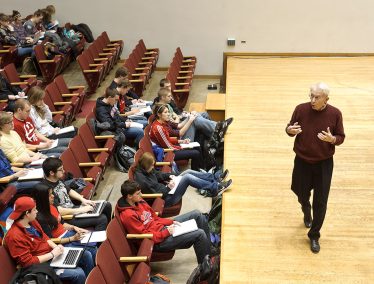 UW Marching Band director, Mike Leckrone, talks in front of a group of students in lecture hall.
