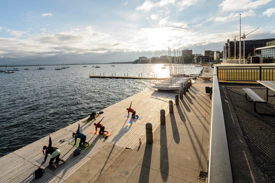 People practicing yoga on wooden deck on the shore of Lake Mendota during sunrise