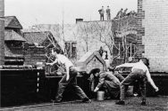 Black and white photo of four male students throwing eggs off of a rooftop.
