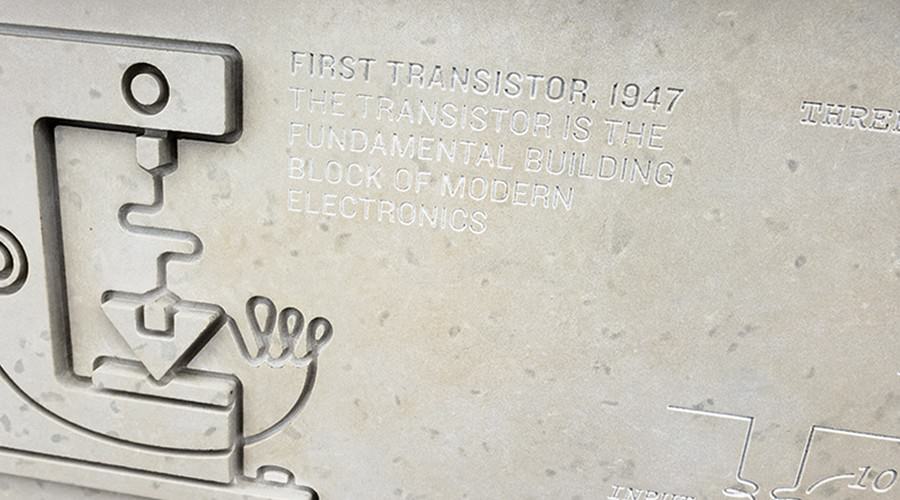 Stone panel with illustration of transistor carved into side along with text "First transistor."