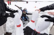 Woman sitting on inflatable inner tube slides into inflatable bowling pins on frozen lake Mendota.