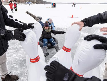 Woman sitting on inflatable inner tube slides into inflatable bowling pins on frozen lake Mendota.