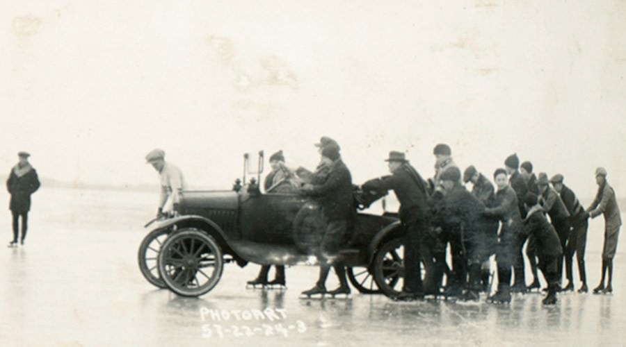Black and white photo of people pushing car on Lake Mendota.