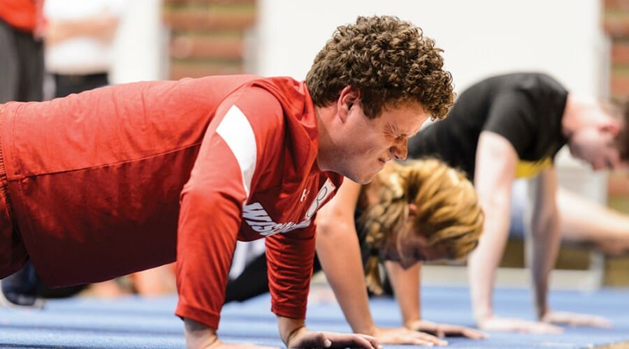 Row of people do push-ups on gym mat.