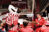 Man with clipboard and Bucky Badger mascot stand in front of group of people.