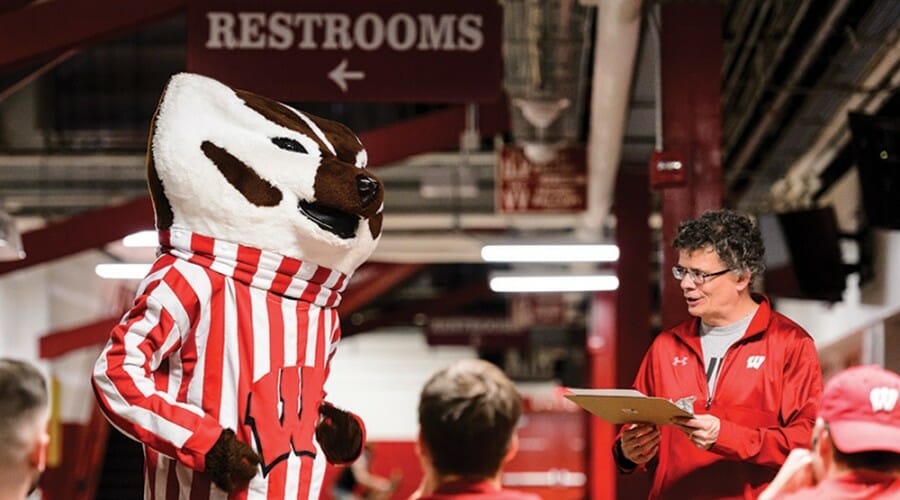 Man with clipboard and Bucky Badger mascot stand in front of group of people.