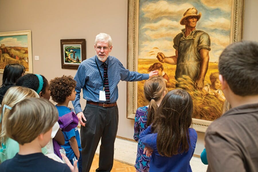 Docent gestures toward large painting in front of group of young children at the Chazen Museum of Art