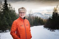 Fran Ulmer stands outdoors against a snowy wooded backdrop with mountains in the distance.