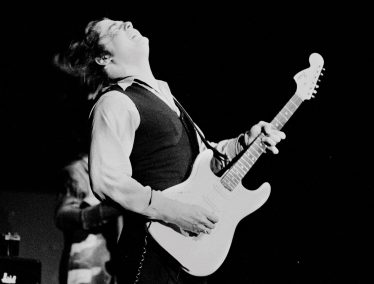 Black and white photo of a young Steve Miller playing electric guitar.