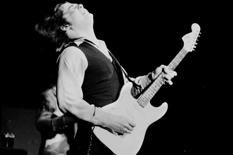 Black and white photo of a young Steve Miller playing electric guitar.