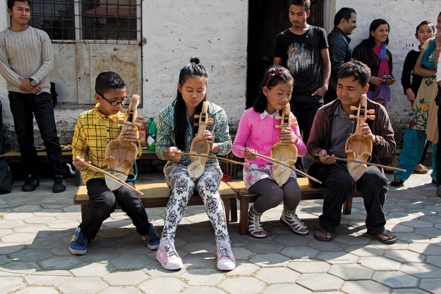 Four children seated on a bench play stringed instruments.