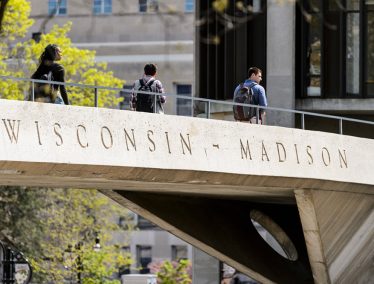 Students walk along pedestrian bridge with words "Wisconsin-Madison" engraved on side.