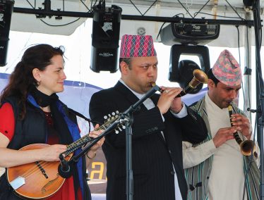 Tara Linhardt plays mandolin on stage alongside two Tibetan musicians.