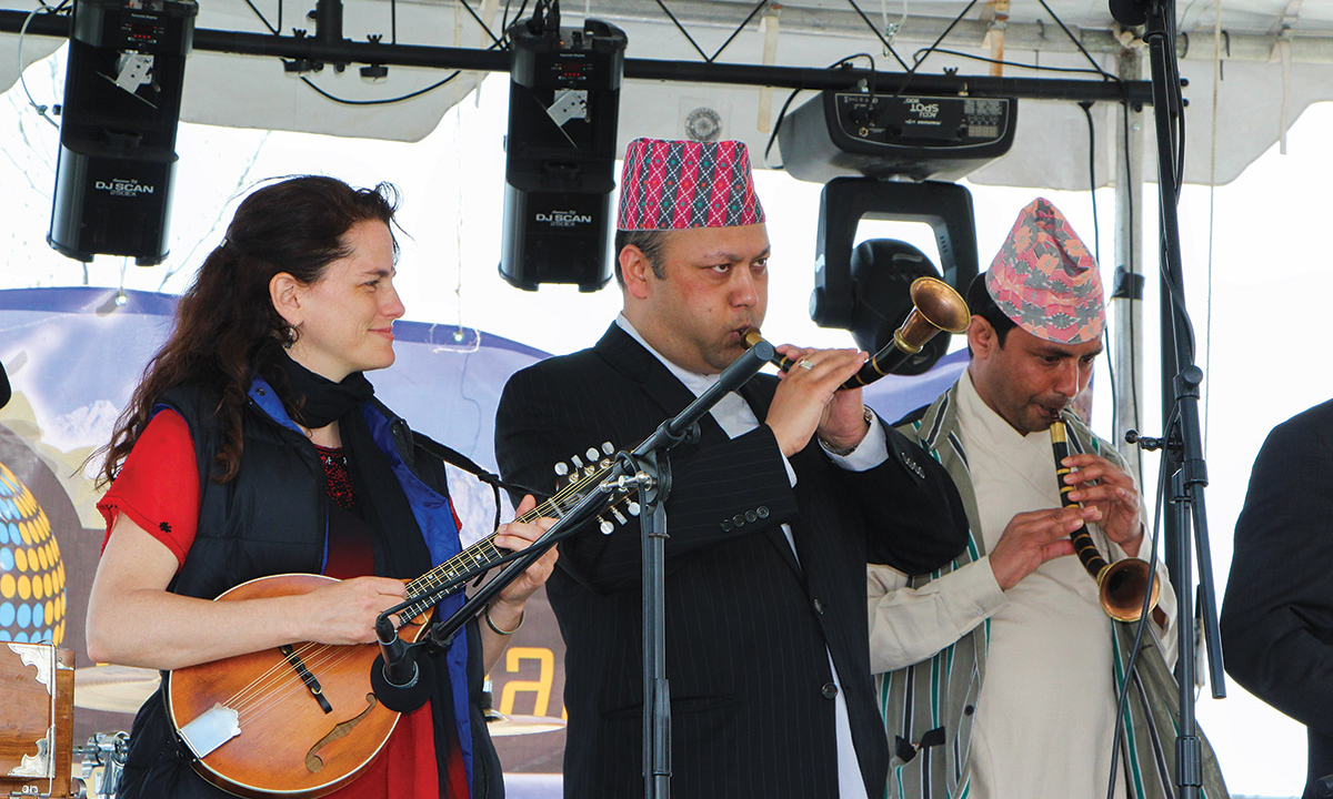 Tara Linhardt plays mandolin on stage alongside two Tibetan musicians.