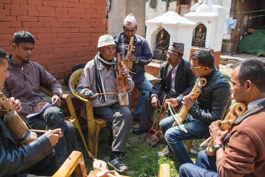 Several Tibetan musicians play instruments together in a circle outside.