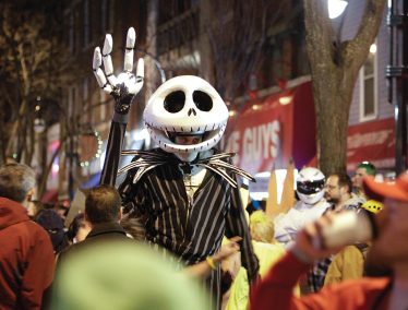 A person wearing a skeleton costume stands among other costumed party-goers on State Street in Madison, Wisconsin