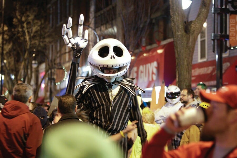 A person wearing a skeleton costume stands among other costumed party-goers on State Street in Madison, Wisconsin