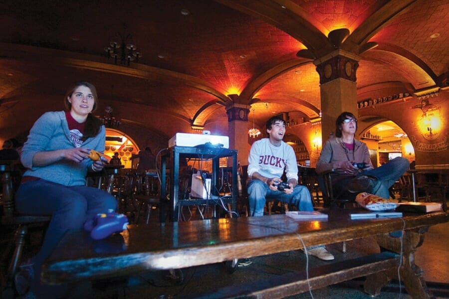 Three students holding video game controllers stare at a screen out of frame