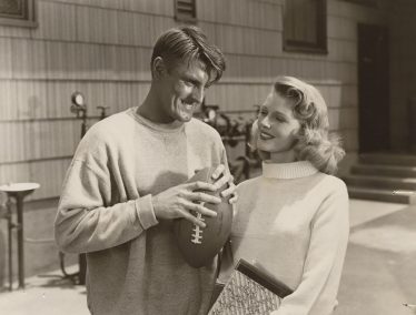 Elroy Hirsch holding a footbal and a female co-star in scene from movie, "Crazylegs"