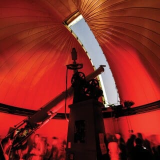 Tourists crowd in the interior of the Washburn Observatory dome that shows a sliver of sky through the open aperture