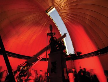 Tourists crowd in the interior of the Washburn Observatory dome that shows a sliver of sky through the open aperture