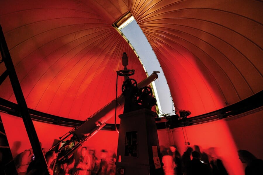 Tourists crowd in the interior of the Washburn Observatory dome that shows a sliver of sky through the open aperture