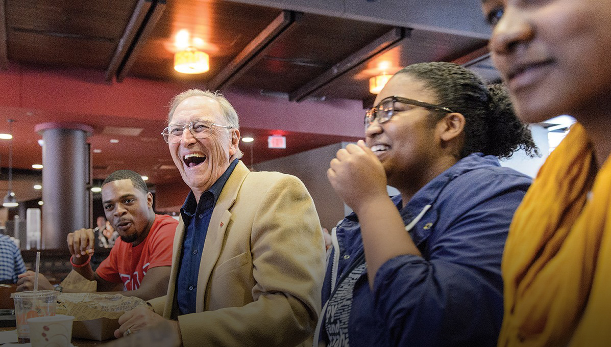 Rod Hassett seated at a table laughing and smiling with a group of students