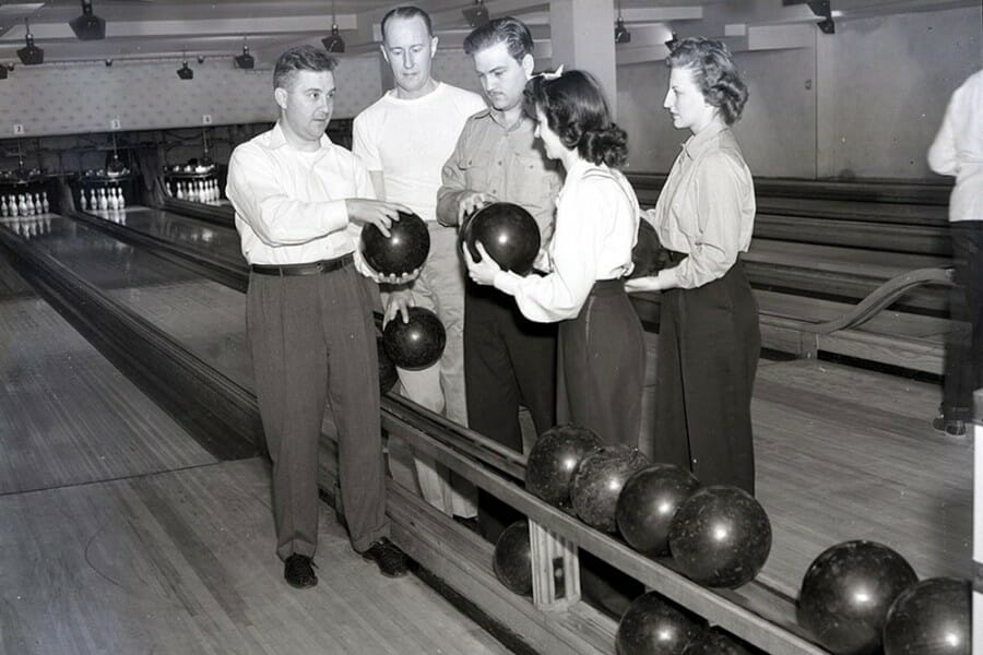 Historical black and white photo of a group of students in a bowling alley holding bowling balls