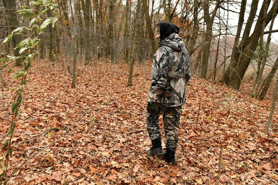 Don Waller walks in woods wearing camouflage