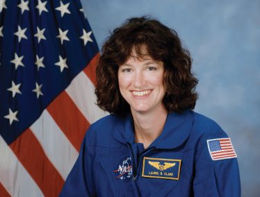 Laurel Clark wearing NASA uniform poses in front of American flag