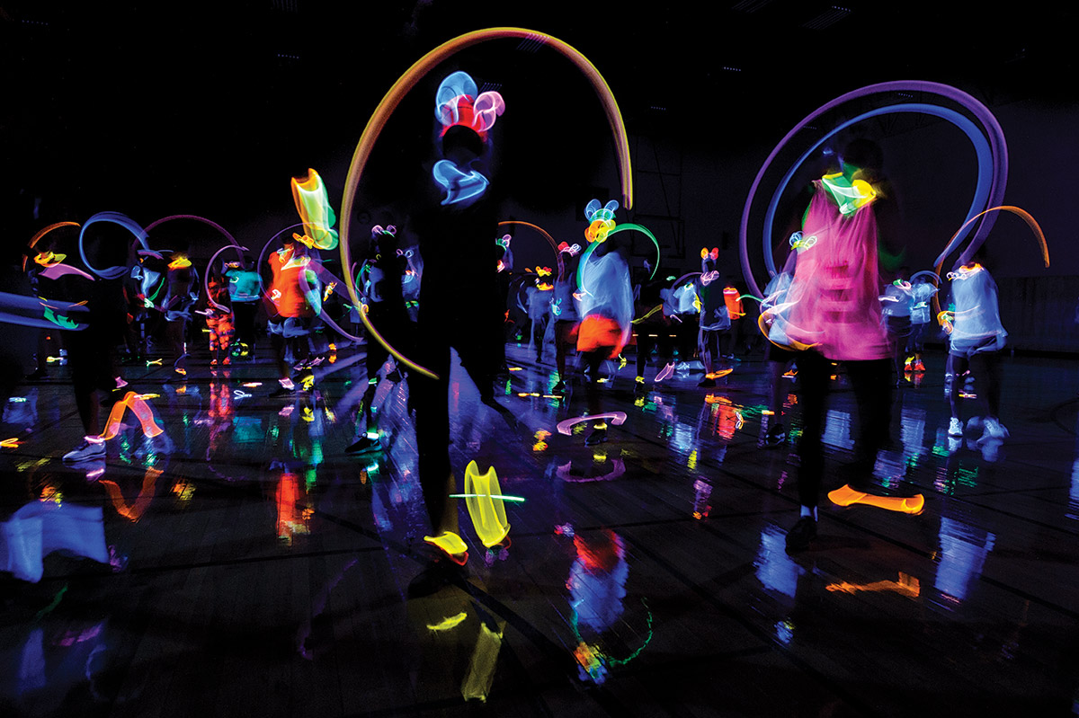 Members of a fitness class move around in a dark gym, wearing glow-in-the-dark accessories