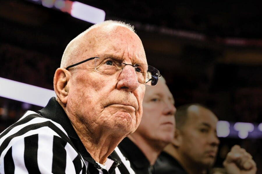 Otto Puls wearing his black and white striped referee uniform watches a basketball game