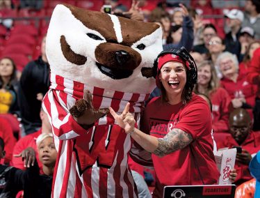 Shawna Nichols wearing her DJ headphones, poses with Bucky Badger during a basketball game