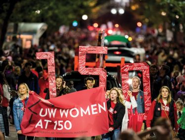 Students march in parade holding banner that reads "UW Women at 150"