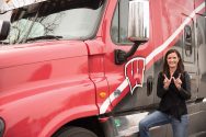 Nancy Spelsburg makes a "W" sign in front of a semi truck with the motion W logo on the side