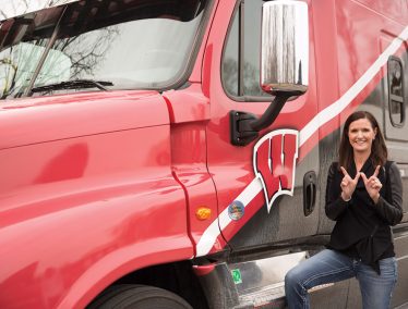 Nancy Spelsburg makes a "W" sign in front of a semi truck with the motion W logo on the side