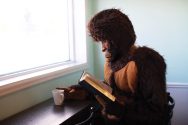 A person wearing a Big Foot costume reads a book with a cup of coffee