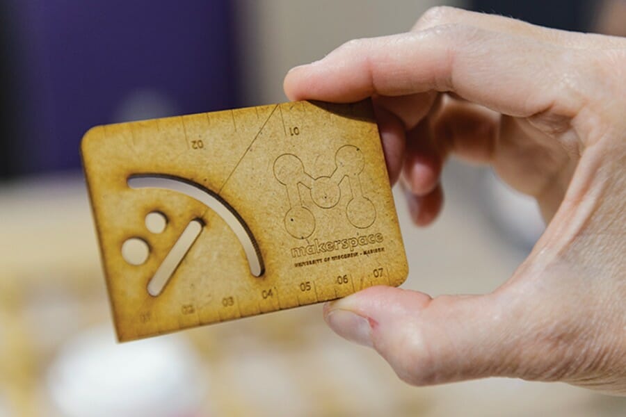 Closeup of person's hand holding a wooden business card featuring the UW Makerspace logo