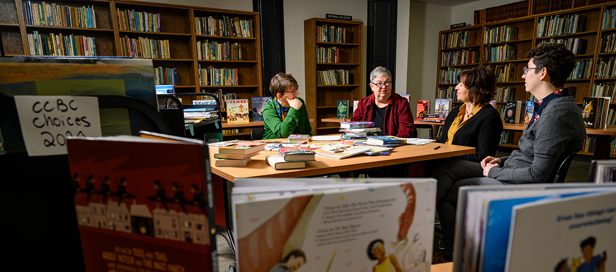 Four librarians engaged in discussion sit around a table surrounded by books